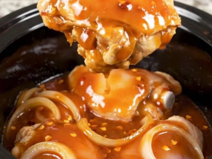 A close-up of tender, braised chicken thighs coated in a rich, dark red honey chipotle sauce with visible onion slices.