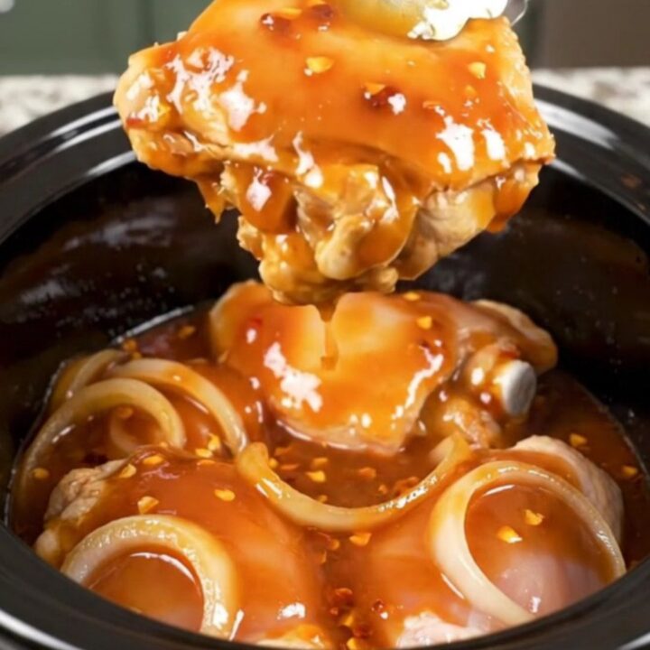 A close-up of tender, braised chicken thighs coated in a rich, dark red honey chipotle sauce with visible onion slices.