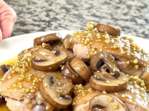 A plate of slow-cooked chicken thighs topped with sautéed mushrooms in a rich garlic butter sauce.