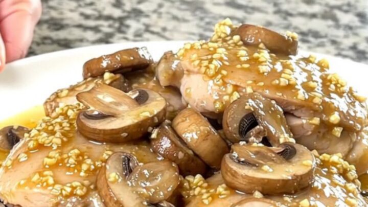 A plate of slow-cooked chicken thighs topped with sautéed mushrooms in a rich garlic butter sauce.