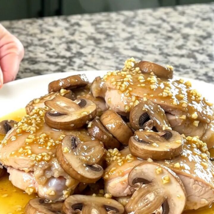 A plate of slow-cooked chicken thighs topped with sautéed mushrooms in a rich garlic butter sauce.