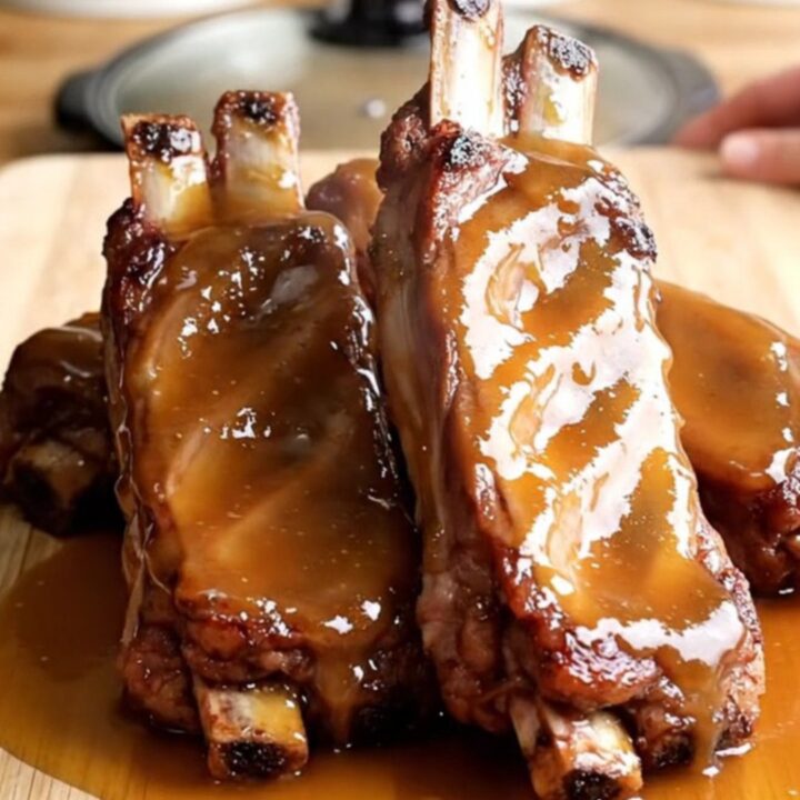 A top-down view of raw sparerib sections arranged in a ring inside a white slow cooker, with corn cobs in the center.