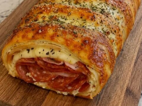 A golden-brown, herb-buttered Stromboli sitting on a wooden cutting board with a visible cheese pull.