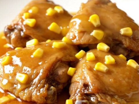 A plate of tender slow-cooked honey butter chicken thighs served with corn kernels and a glossy sauce.