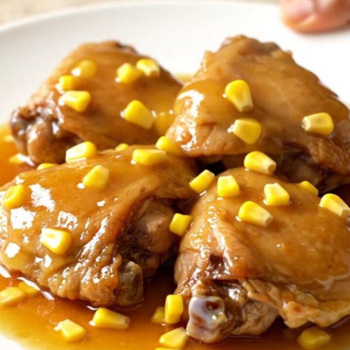 A plate of tender slow-cooked honey butter chicken thighs served with corn kernels and a glossy sauce.