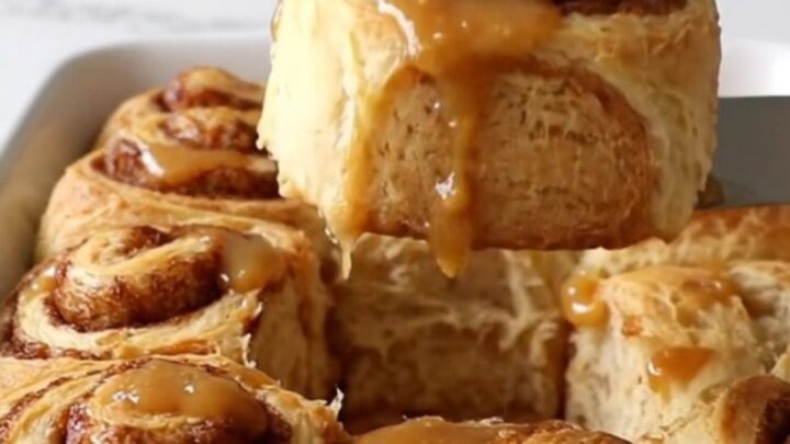 A top-down view of twelve raw cinnamon roll dough rounds arranged in a white rectangular ceramic baking dish.