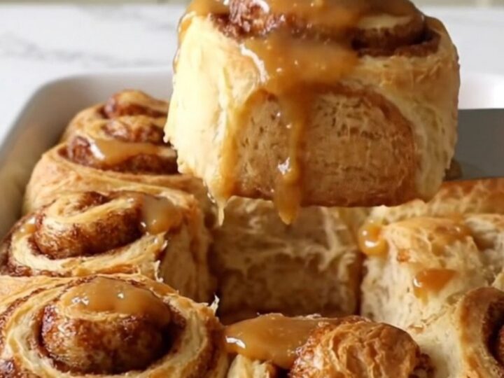 A top-down view of twelve raw cinnamon roll dough rounds arranged in a white rectangular ceramic baking dish.
