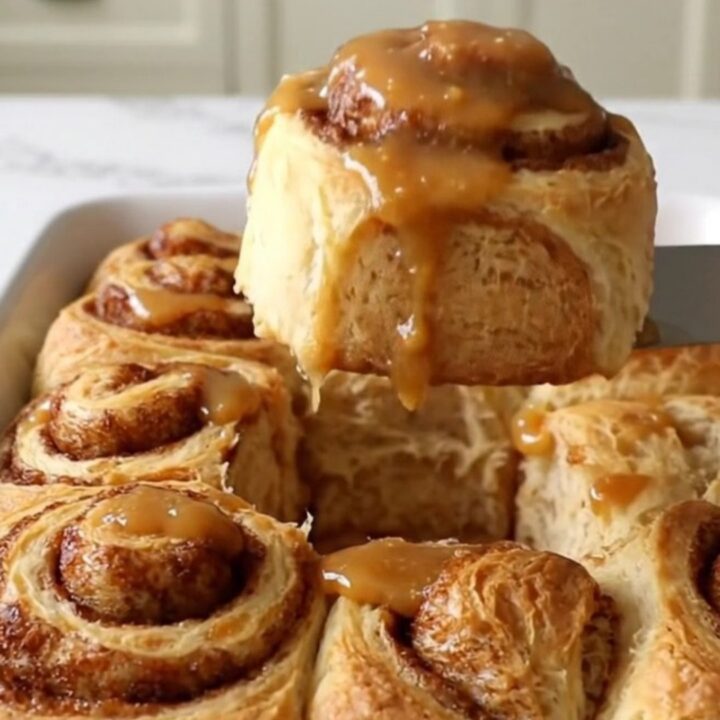 A top-down view of twelve raw cinnamon roll dough rounds arranged in a white rectangular ceramic baking dish.