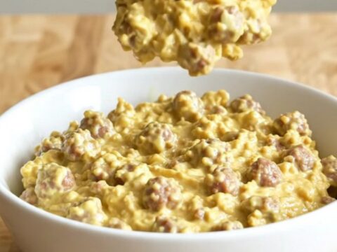 A creamy, steaming sausage dip in a white ceramic slow cooker, garnished with herbs.