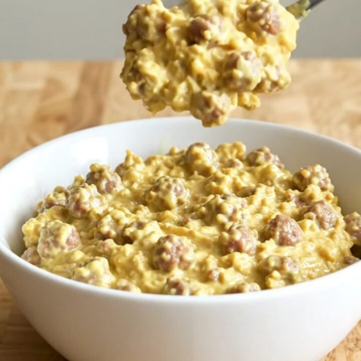 A creamy, steaming sausage dip in a white ceramic slow cooker, garnished with herbs.