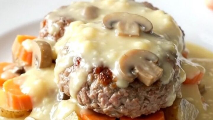 A close-up view of a slow cooker filled with beef patties, sliced gold potatoes, and carrots in a creamy mushroom gravy.