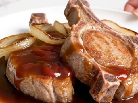 Five raw boneless pork chops arranged in a black slow cooker insert on a white speckled quartz countertop.