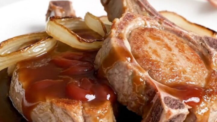 Five raw boneless pork chops arranged in a black slow cooker insert on a white speckled quartz countertop.