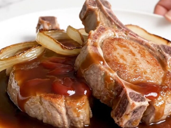 Five raw boneless pork chops arranged in a black slow cooker insert on a white speckled quartz countertop.