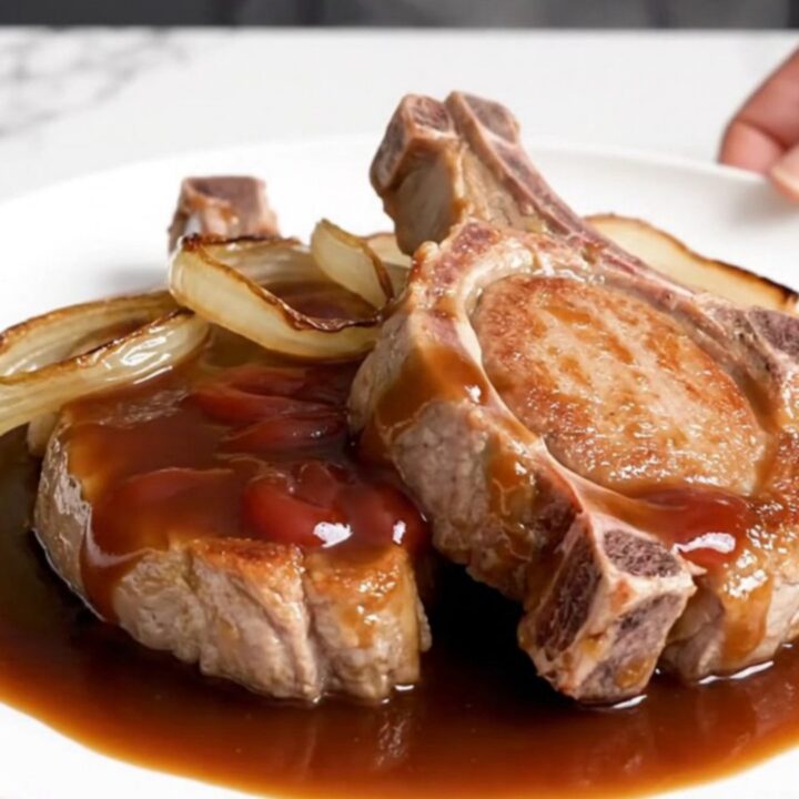 Five raw boneless pork chops arranged in a black slow cooker insert on a white speckled quartz countertop.