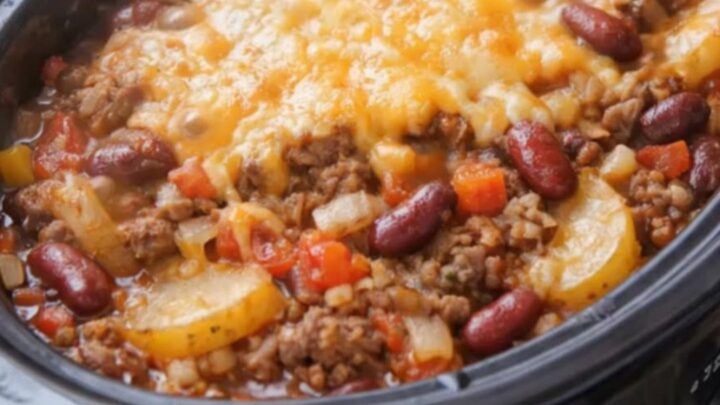 A hot slow cooker filled with cowboy casserole showing melted bubbly cheddar cheese on top