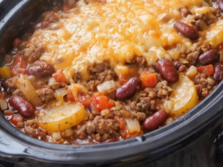 A hot slow cooker filled with cowboy casserole showing melted bubbly cheddar cheese on top