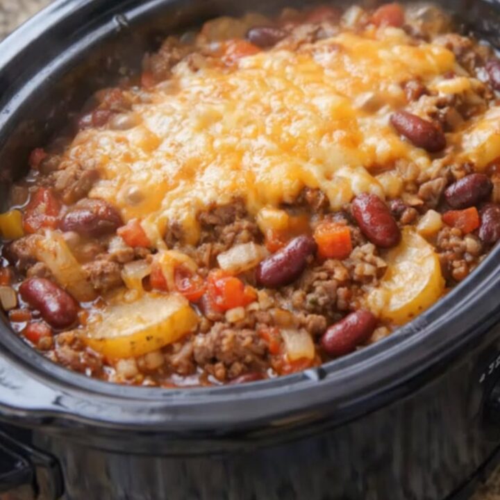 A hot slow cooker filled with cowboy casserole showing melted bubbly cheddar cheese on top