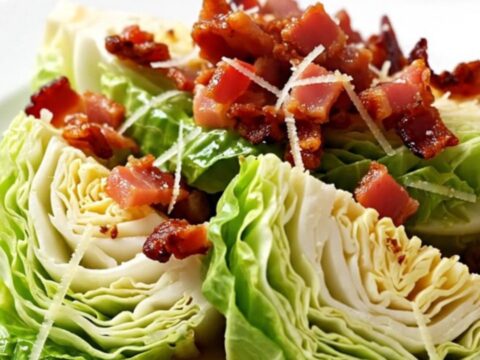 A top-down view of green cabbage wedges in a slow cooker topped with bacon and parmesan.