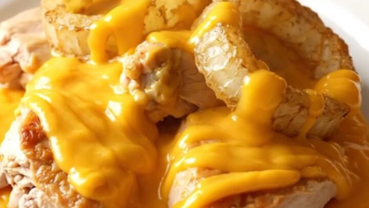 A close-up shot of tender braised chicken thighs topped with sweet onions and a creamy cheddar sauce in a slow cooker.