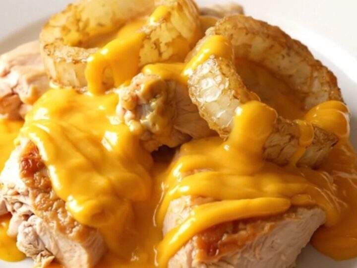 A close-up shot of tender braised chicken thighs topped with sweet onions and a creamy cheddar sauce in a slow cooker.