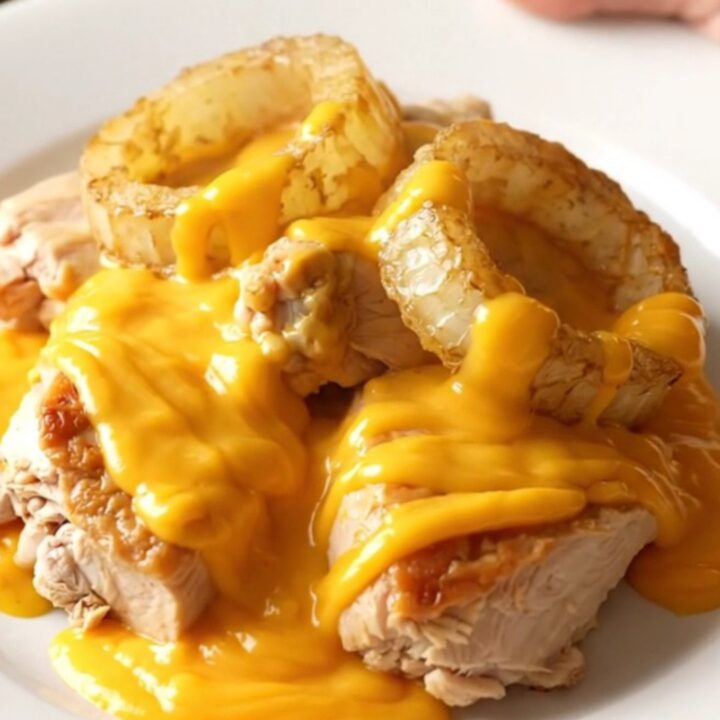 A close-up shot of tender braised chicken thighs topped with sweet onions and a creamy cheddar sauce in a slow cooker.