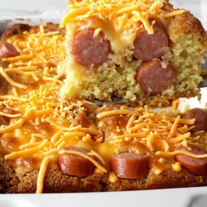 A golden-brown corn dog cornbread casserole in a white ceramic dish on a quartz countertop.