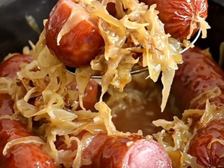 A close-up view of thick chunks of smoked kielbasa served on a bed of golden, soft sauerkraut in a slow cooker.