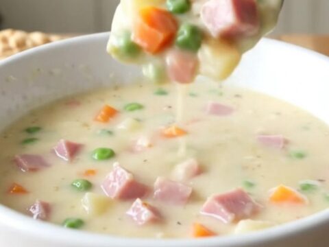 A white bowl filled with creamy ham and potato soup on a rustic wooden table.