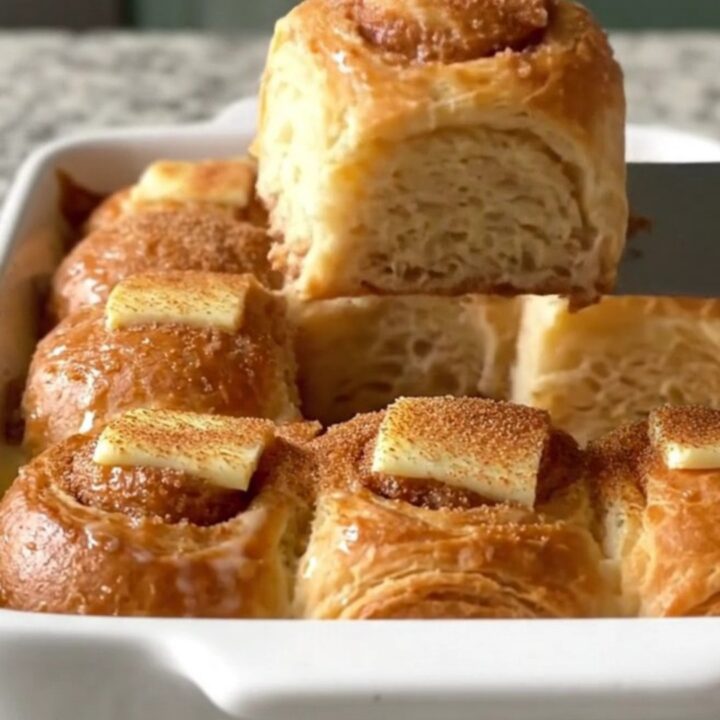 A golden-brown Hawaiian roll French toast bake in a white ceramic dish on a speckled countertop.