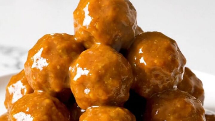 A top-down view of honey buffalo turkey meatballs simmering in a black slow cooker on a white speckled countertop.