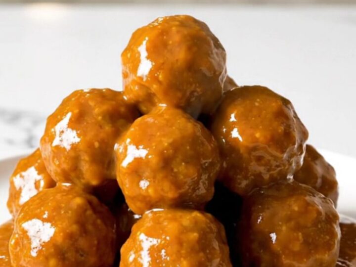 A top-down view of honey buffalo turkey meatballs simmering in a black slow cooker on a white speckled countertop.