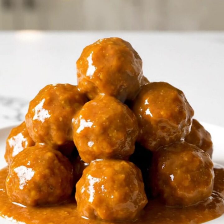 A top-down view of honey buffalo turkey meatballs simmering in a black slow cooker on a white speckled countertop.