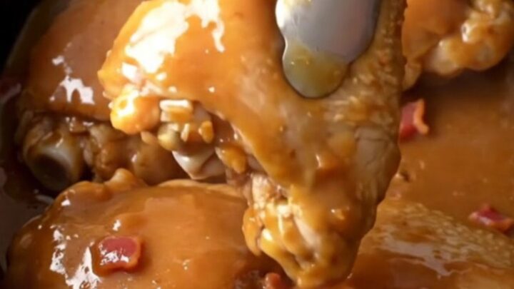 Slow cooker chicken thighs glazed in a rich brown sugar, butter, and bacon sauce in a stoneware insert.
