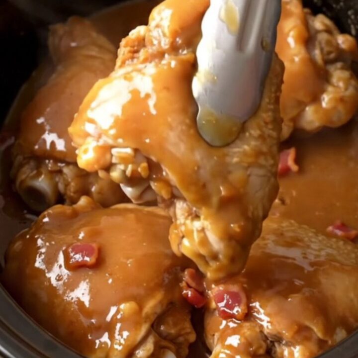 Slow cooker chicken thighs glazed in a rich brown sugar, butter, and bacon sauce in a stoneware insert.