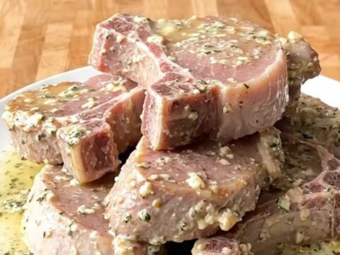 A top-down view of tender pork chops slow-cooked in a creamy garlic and herb sauce in a white ceramic slow cooker.