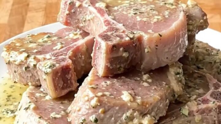 A top-down view of tender pork chops slow-cooked in a creamy garlic and herb sauce in a white ceramic slow cooker.