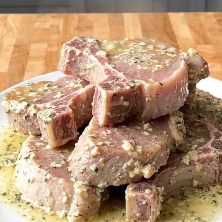A top-down view of tender pork chops slow-cooked in a creamy garlic and herb sauce in a white ceramic slow cooker.