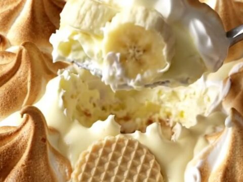 A warm, golden-brown baked banana pudding in a ceramic dish, showing toasted meringue peaks.