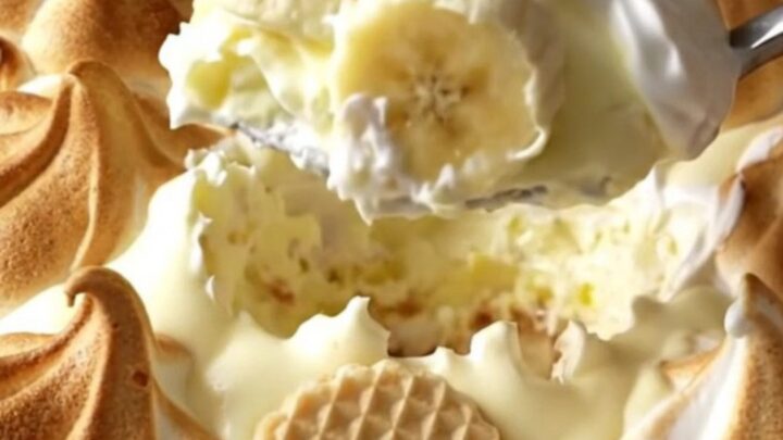 A warm, golden-brown baked banana pudding in a ceramic dish, showing toasted meringue peaks.