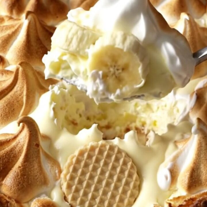 A warm, golden-brown baked banana pudding in a ceramic dish, showing toasted meringue peaks.