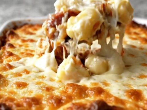 A top-down view of a rectangular white baking dish filled with potato gnocchi, smoked sausage, Alfredo sauce