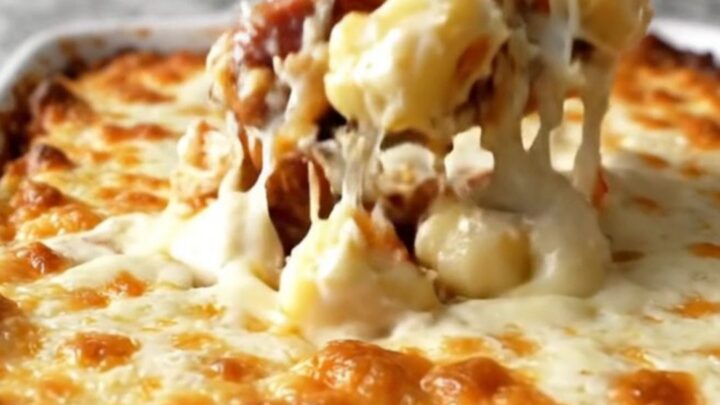 A top-down view of a rectangular white baking dish filled with potato gnocchi, smoked sausage, Alfredo sauce