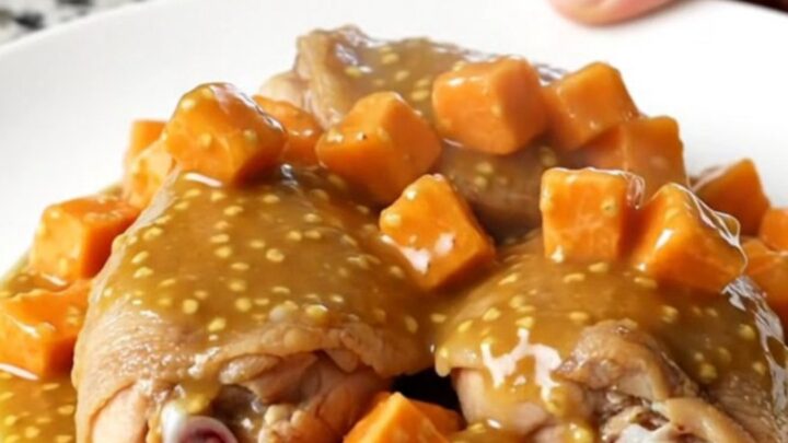 A close-up of tender chicken thighs and cubed sweet potatoes coated in a glossy honey mustard sauce in a slow cooker.