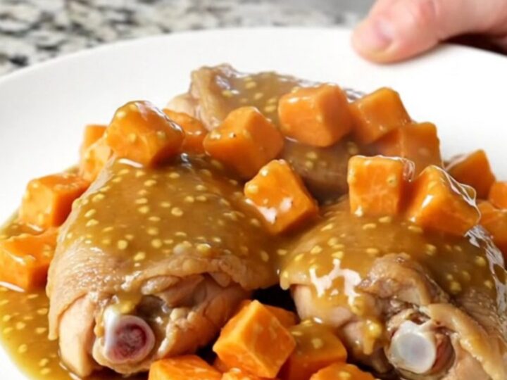 A close-up of tender chicken thighs and cubed sweet potatoes coated in a glossy honey mustard sauce in a slow cooker.