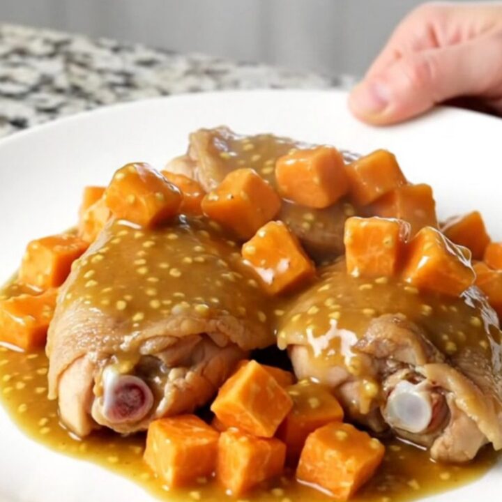A close-up of tender chicken thighs and cubed sweet potatoes coated in a glossy honey mustard sauce in a slow cooker.