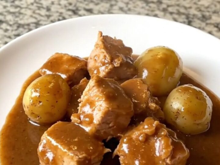 A close-up of tender turkey cubes and baby gold potatoes in a rich brown gravy inside a slow cooker.