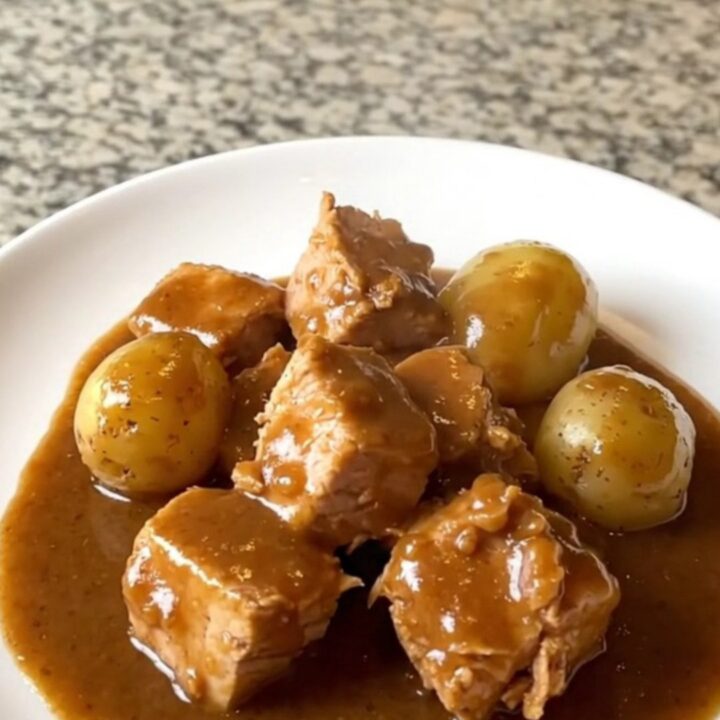 A close-up of tender turkey cubes and baby gold potatoes in a rich brown gravy inside a slow cooker.
