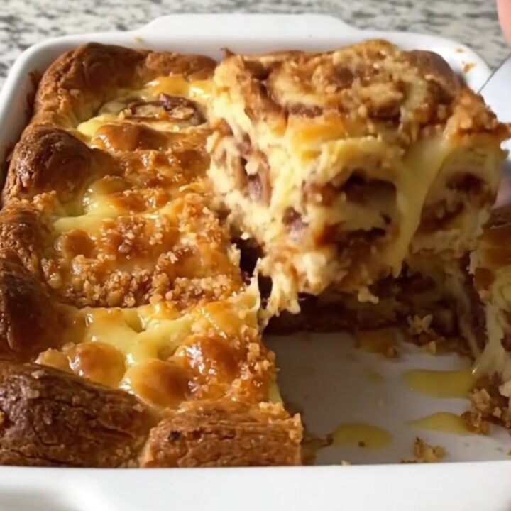 A golden brown eggnog cinnamon roll bake in a white ceramic dish on a speckled countertop.