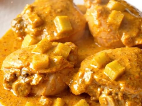 A close-up shot of creamy buffalo chicken thighs served on a white plate with visible celery pieces.